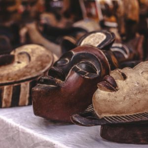 Carved wooden masks with intricate designs displayed at a vibrant market.